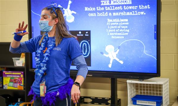 teacher stands in front of room and explains STEM challenge